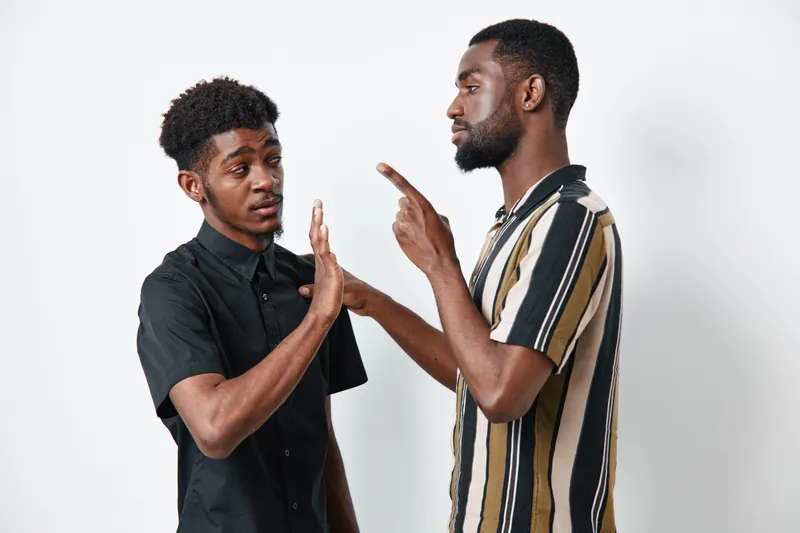 Two African American men with dark skin having a serious conversation on white background. One man gestures with finger while the other raises hand in refusal or stop sign.