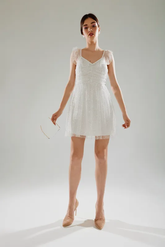 Young woman in a white lace dress poses confidently in a studio with neutral background. Concept of beauty, fashion, elegance, and modern style for clothing and lifestyle.