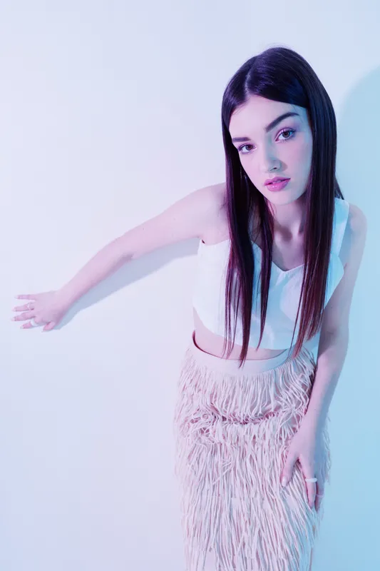 Young woman beauty fashion model with long dark hair wearing a white top and textured skirt posing against a light background. Concept for style and elegance.