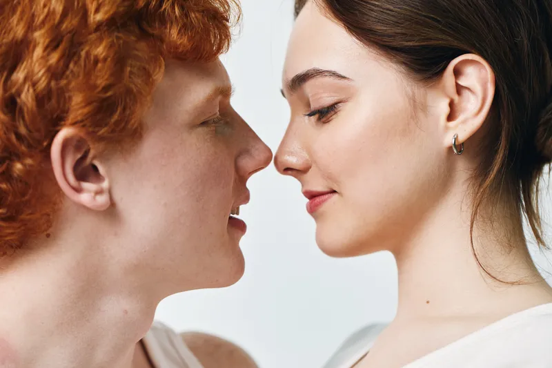 Young man and woman close face to face with eyes closed and slight smile for intimacy connection and affection in studio light background. Love and relationship concept.