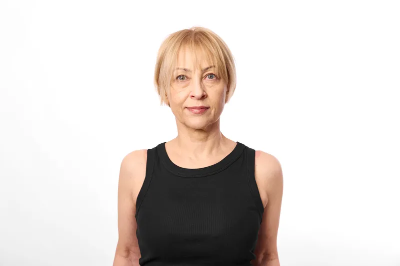 Woman portrait of a senior elderly blonde with short hair, wearing black sleeveless dress, neutral expression, studio lighting, white background