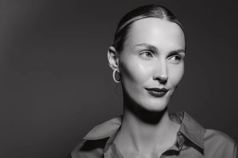 Portrait of a fair skinned Caucasian woman with slicked hair and hoop earrings looking aside. Studio lighting highlights her smooth skin and confident expression.