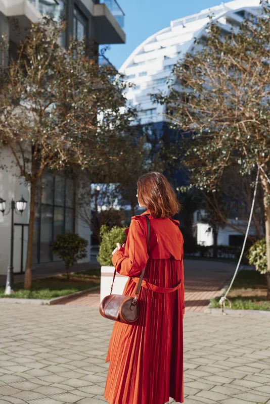 Woman in red dress stands outdoors in an urban city plaza, back to camera, capturing fashion mood and street style against modern architecture