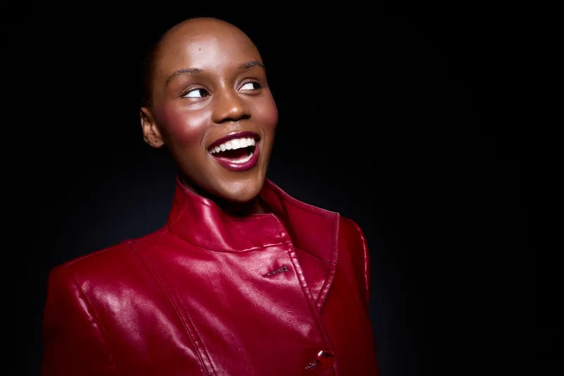 Smiling dark skinned African woman in red leather jacket looks away with bright joyful expression. Studio portrait with black background. Concept of fashion, confidence, and happiness.