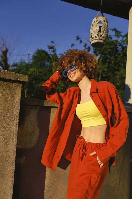 Woman lifestyle outdoor portrait, wearing red jacket and yellow top, relaxed pose by a wall, casual fashion vibe, cheerful mood, candid style, warm lighting, carefree attitude