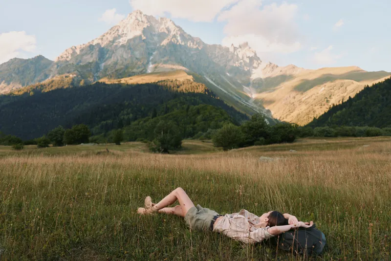 Woman rests on a grassy field with distant mountains, capturing a relaxed outdoor lifestyle moment in a natural landscape with a calm mood and open space.