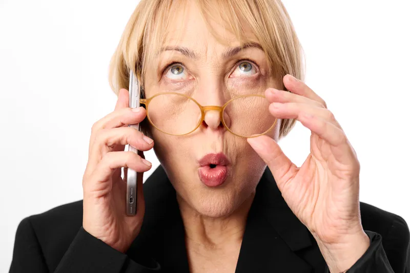 Woman, senior, glasses, phone communication, surprised studio portrait of elderly female adjusting eyewear with hands, holding smartphone near ear, white background