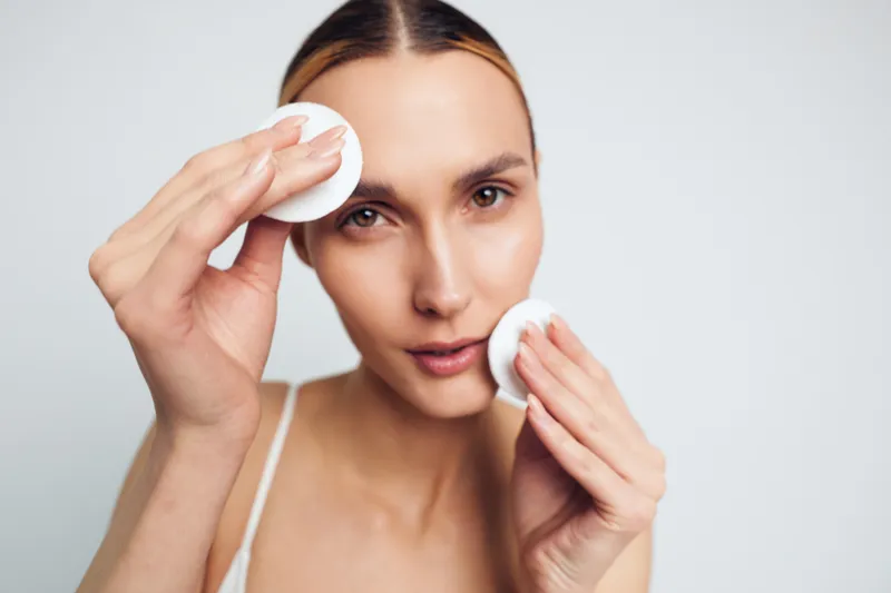 Woman skincare face cleansing with cotton pad, gently wiping eye and cheek, makeup removal, calm natural expression, beauty routine in studio light background, hygienic cotton for fresh clear