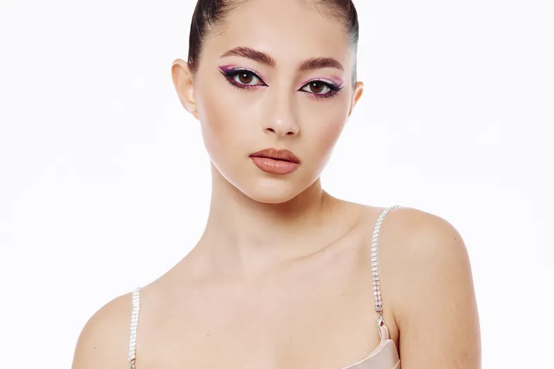 Young woman with creative fashion makeup featuring bold eyeliner and glossy lips poses on a white background. Concept focuses on beauty, style, and cosmetics.
