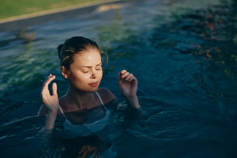 Calm woman swims in clear pool with eyes closed, enjoying a peaceful moment, soft light on water, relaxed posture, lifestyle scene capturing leisure and wellness in a tranquil aquatic setting
