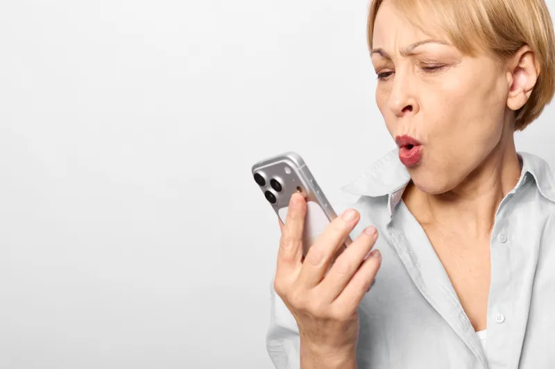 Woman surprised closeup portrait, holding smartphone near face, mouth open in shock, reacting to incoming message, modern communication concept, isolated on white background