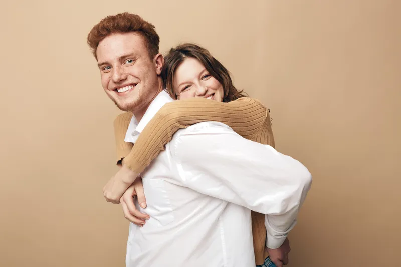 Happy young couple in casual clothes smiling and embracing each other against beige background. Concept of love, friendship, relationship, and joyful moments together.