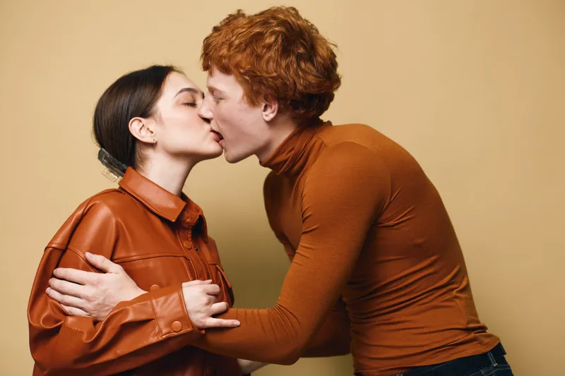 Couple kissing with closed eyes and tender emotions, man and woman embracing each other against neutral background, love and affection in casual clothing close-up.