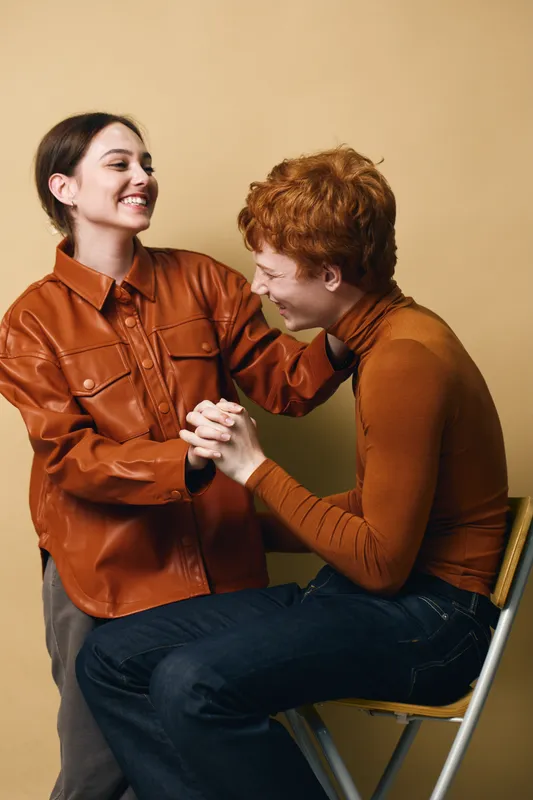 Young couple smiling and holding hands together in casual autumn clothes with warm colors background. Friends enjoying moment with happiness and connection indoors.