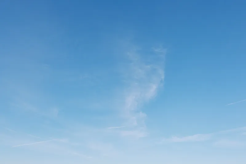 Blue sky with delicate wispy clouds stretching across an open expanse, clear atmosphere and bright daylight. A tranquil, minimal scene suitable for travel, outdoor, or nature backgrounds.
