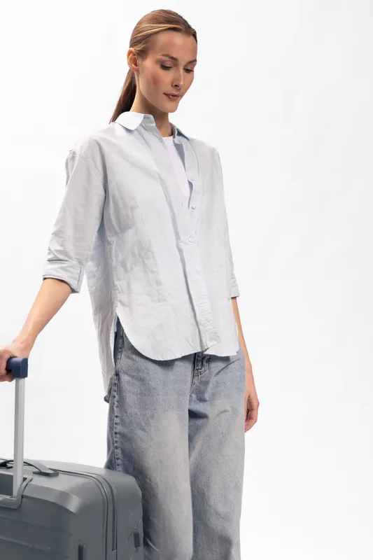 Young woman in casual outfit stands with suitcase on white background. Concept for travel, journey, vacation preparation, and lifestyle with luggage and fashion.