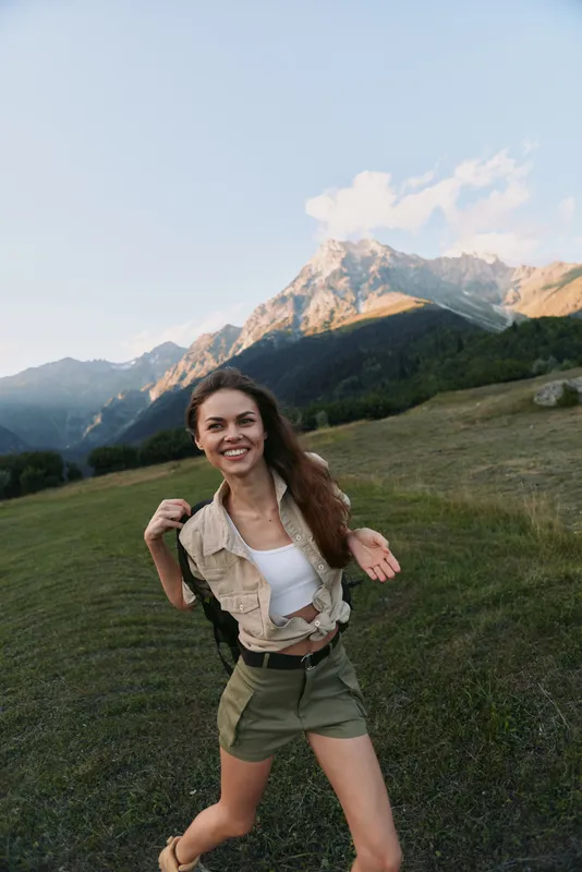 Happy young woman hiking in mountains wearing casual outfit enjoys nature and fresh air with smiling face and positive lifestyle outdoors during sunny day.