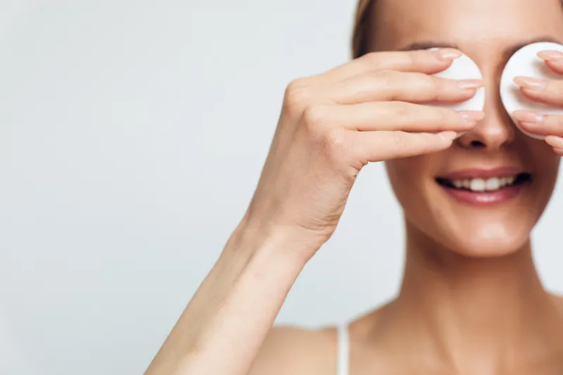 Woman, skincare, face, cream, selfcare, wellness, closeup, smiling, applies white cream with fingertips covering eyes, soft studio lighting, clean background, skincare routine, gentle hydration