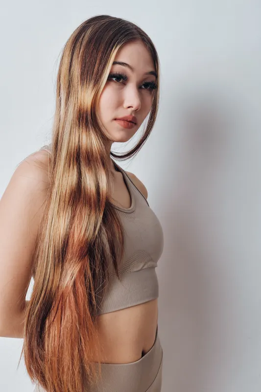 Woman with long straight hair wearing crop top and skirt standing against white background looking aside with neutral expression in casual fashion portrait studio shot.
