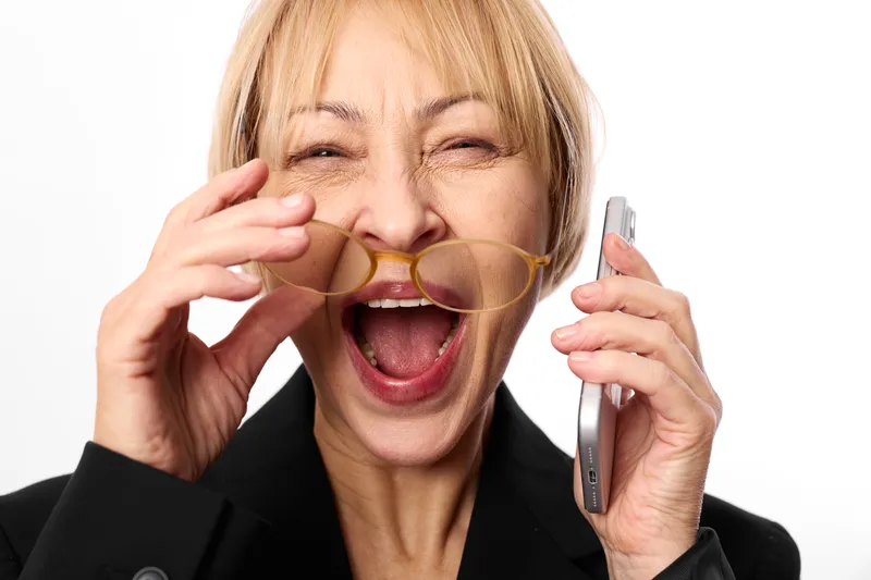 Stressed businesswoman with phone in hand shows burnout, communication overload, multitasking pressure, anxiety and panic during work, eyes closed and mouth open, white background