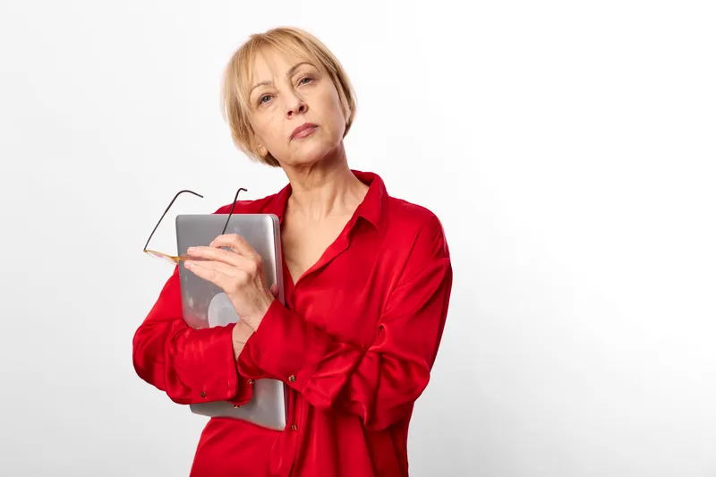 Senior woman, red shirt, holding document package, presentation pose in studio, calm thoughtful expression, white background, copy space for text, modern lifestyle, portrait