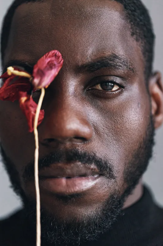 African man portrait with dried red flower in creative conceptual style closeup, dark skin, facial details, artistic expression, visual art, isolated background, studio lighting