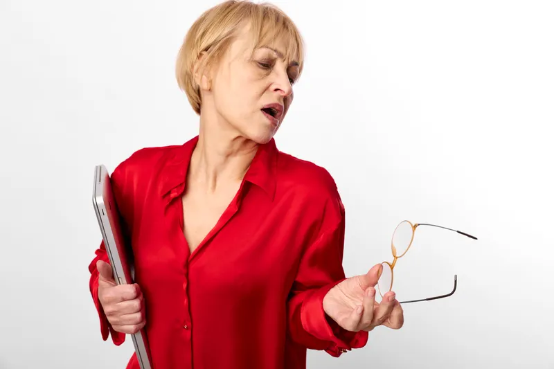woman with red blouse holding glasses, eyewear for vision, eye tired expression, she looks concerned with closed eyes, studio white background, soft lighting, portrait concept