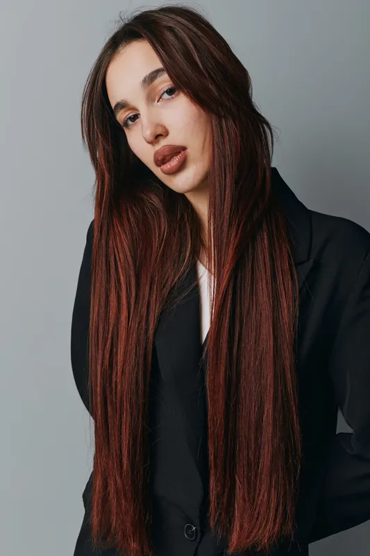 Woman with long straight hair and natural makeup wearing black blazer posing against gray background for fashion portrait and beauty concept in studio lighting.