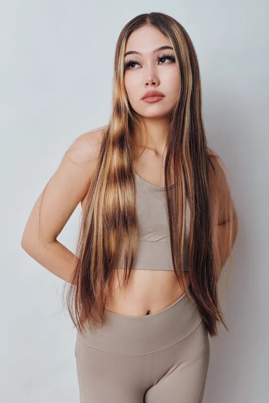 Young woman with long straight hair wearing brown crop top and pants posing indoors on light background. Beauty, fashion and casual style with confident expression for portrait.