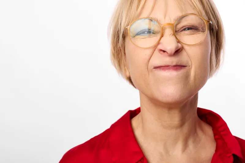 Woman with glasses, senior tired expression, stress, sadness and worry in portrait against plain white background, soft daylight, red top, close view of mature face.