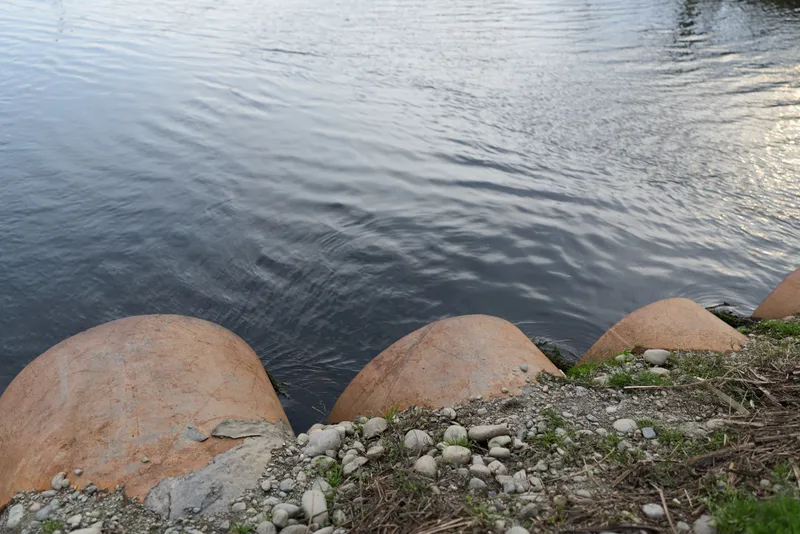 Rippling river water beside rounded stones and rocks on a natural shoreline, rocky edge with small plants, calm outdoor landscape, peaceful nature lifestyle, soft light for relaxation