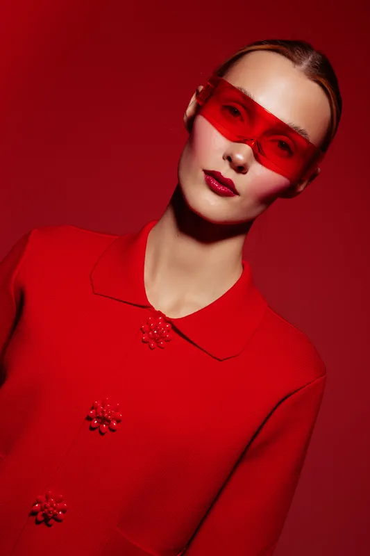 Fashion model in red outfit and red translucent glasses poses on red background. Concept of modern style, bold color, and futuristic eyewear in studio portrait.