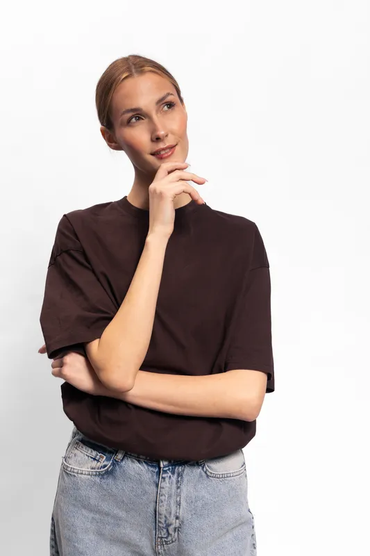 Thoughtful young woman in casual clothes looks up and touches chin against white background. Concept of contemplation, decision making, and positive mood in everyday life.