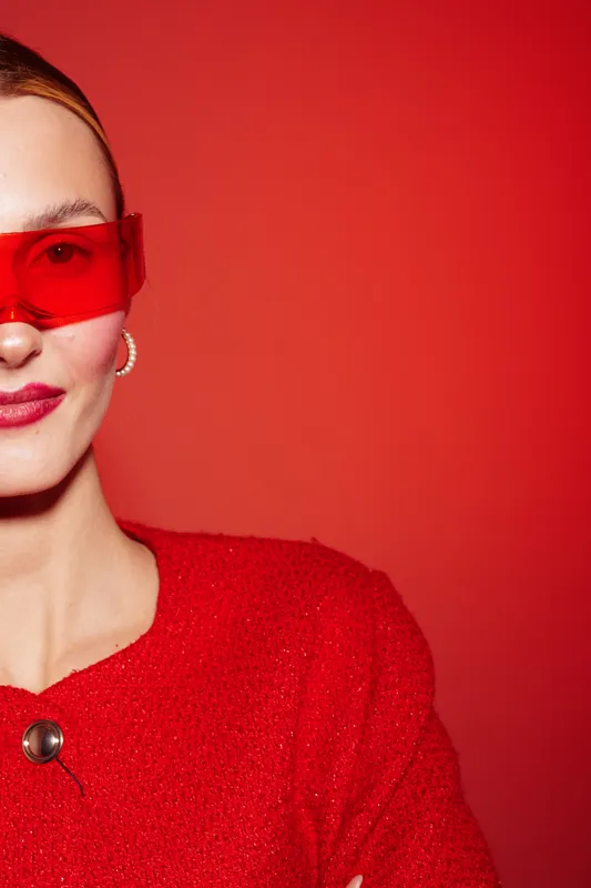 Stylish woman in red sweater and red sunglasses poses confidently against red background. Fashion portrait with modern accessories and bold color contrast for trendy style concept.