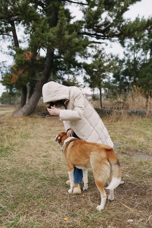 Dog and person share a quiet outdoors moment, a warm winter coat embracing them as they greet in a grassy park setting.