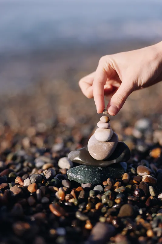 Balance, stones, stack, zen on a pebbled beach as a hand arranges smooth rocks into a tiny tower, capturing calm, focus and natural harmony in nature and serenity for reflection.