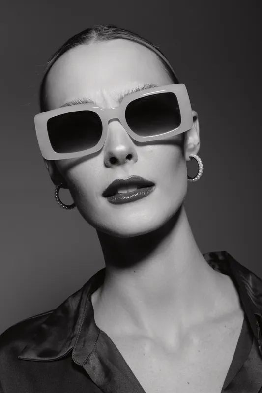 Portrait of a pale skinned Caucasian woman wearing large square sunglasses and hoop earrings in black and white. Fashion concept with stylish accessories and modern attitude.