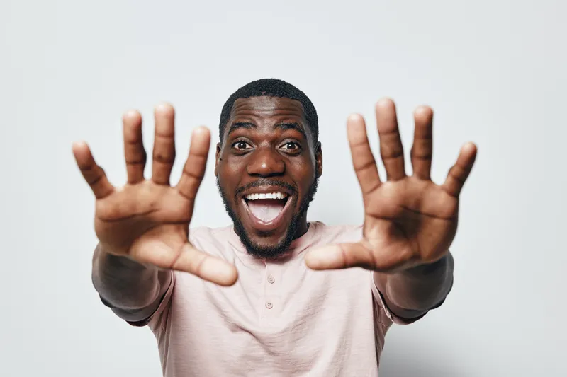 African man with dark skin and beard smiling and showing hands forward with open palms on white background. Happy male portrait with excitement and positive emotion in studio.