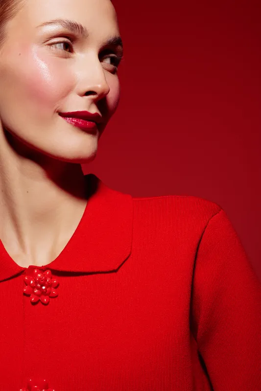 Close-up of a smiling woman with red lipstick wearing a red sweater against a red background. Concept of fashion, beauty, makeup, and confident style.