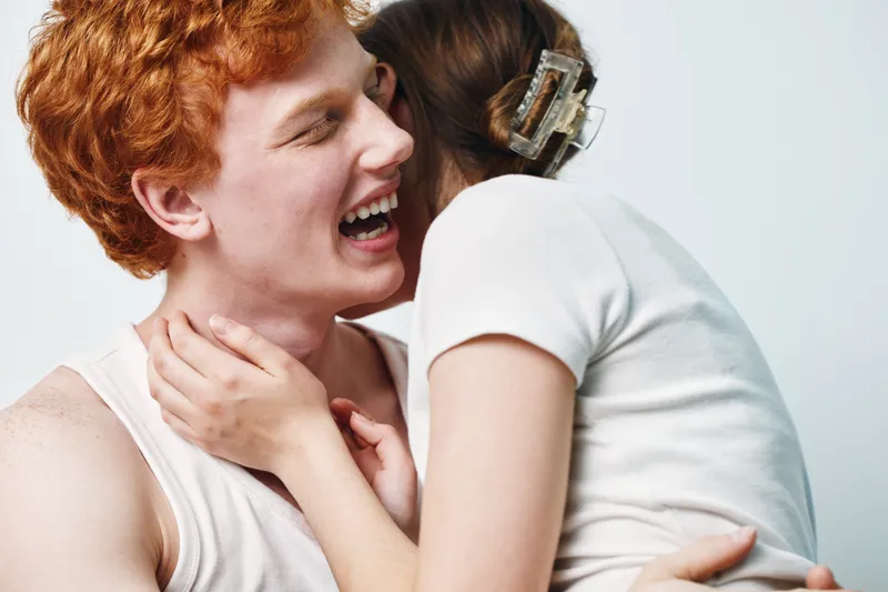 Couple hugging and laughing together in close embrace with white background, showing affection, happiness, connection, love, and intimacy between man and woman.