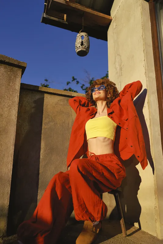woman lifestyle outdoor fashion casual pose sunny confident on a terrace beneath a lantern, a bright red tracksuit with a yellow top showcasing bold street style