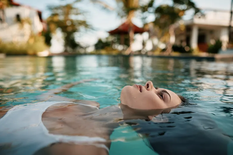 pool, woman, float, relaxation, outdoor poolside scene shows a woman floating serenely in sunlit water, conveying leisure, vacation mood, gentle breeze, tranquil reflections, calm atmosphere and warm