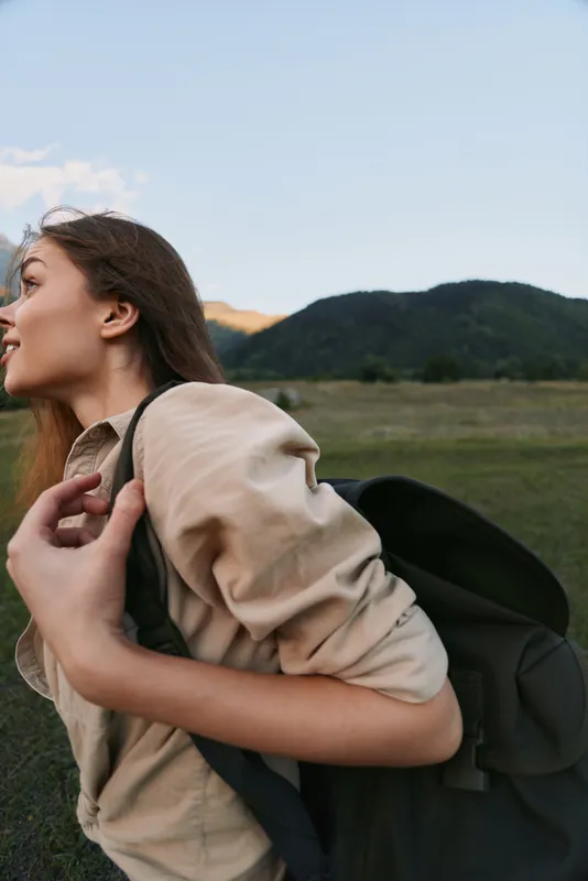 A woman hiker outdoors with a backpack, moving along a grassland landscape, capturing independence, adventure, and an active lifestyle in nature.