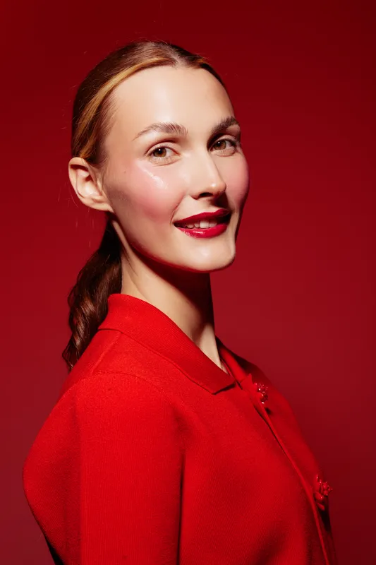 Portrait of a smiling woman with shiny skin and red lipstick wearing a red outfit against a red background. Concept of beauty, fashion, makeup, and confident expression.