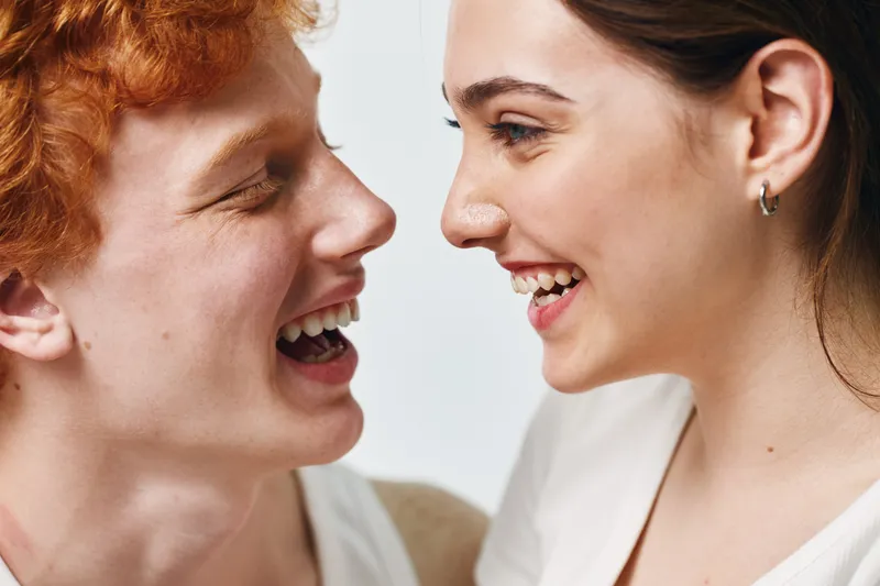 Young man and woman smiling face to face in closeup portrait with happy expression. People laughing and looking at each other with joy and friendship on white background.