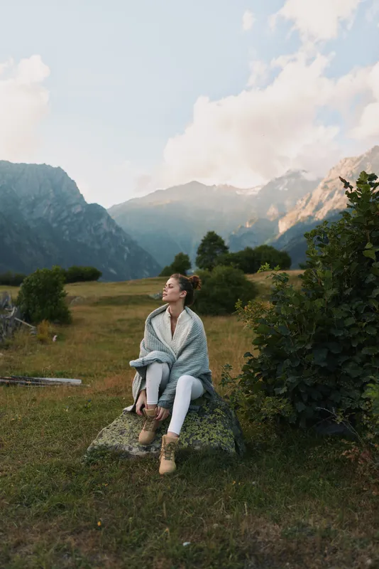 Young woman lifestyle sitting on rock outdoors in mountains enjoying fresh air peaceful moment casual outfit natural light scenic background