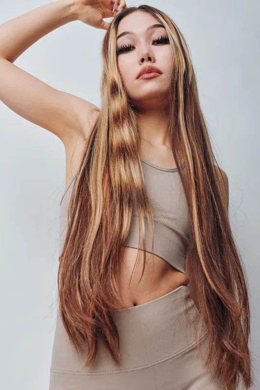 Young woman with long straight hair posing in beige crop top and matching pants against gray background. Fashion, beauty, confident model with natural makeup and casual outfit.