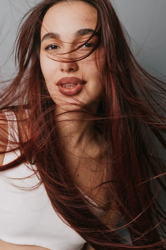 Young woman with long hair and natural makeup posing with hair flowing around her face in white top against neutral background. Beauty, portrait and style with casual expression.