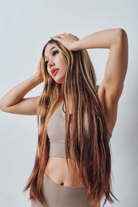 Young woman with long straight hair posing in casual sleeveless crop top and skirt. Beauty portrait with natural makeup, expressive face and light gray background studio shot.
