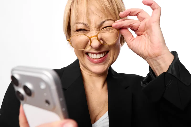 Woman smiling, senior business portrait, adjusting glasses with one hand, looking at smartphone, white studio background, expression, communication tech